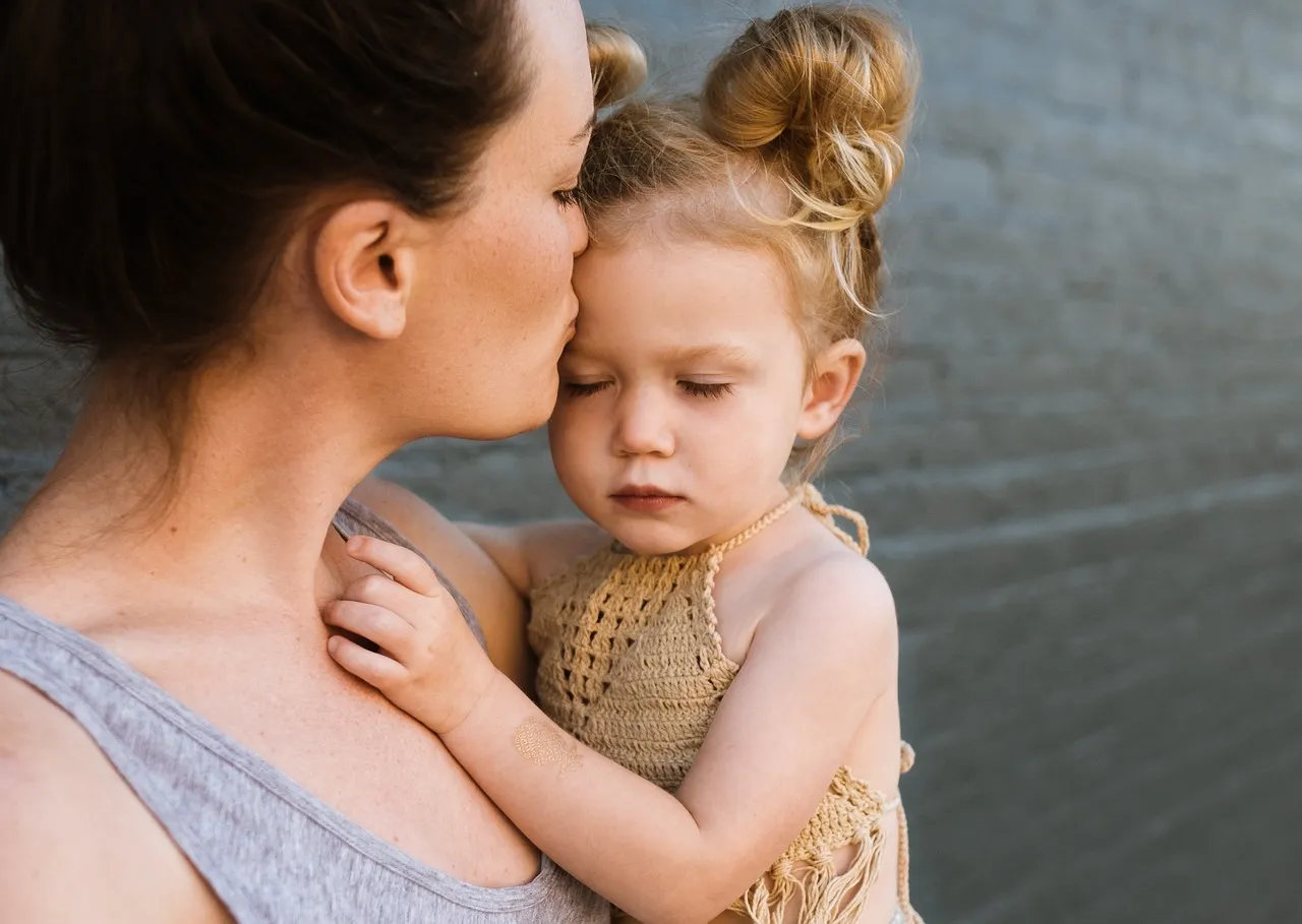 Mutter küsst ihre kleine Tochter auf die Stirn